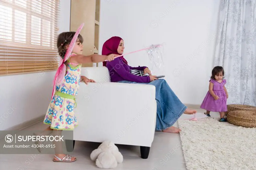 Mother holding the television remote control, daughters playing around
