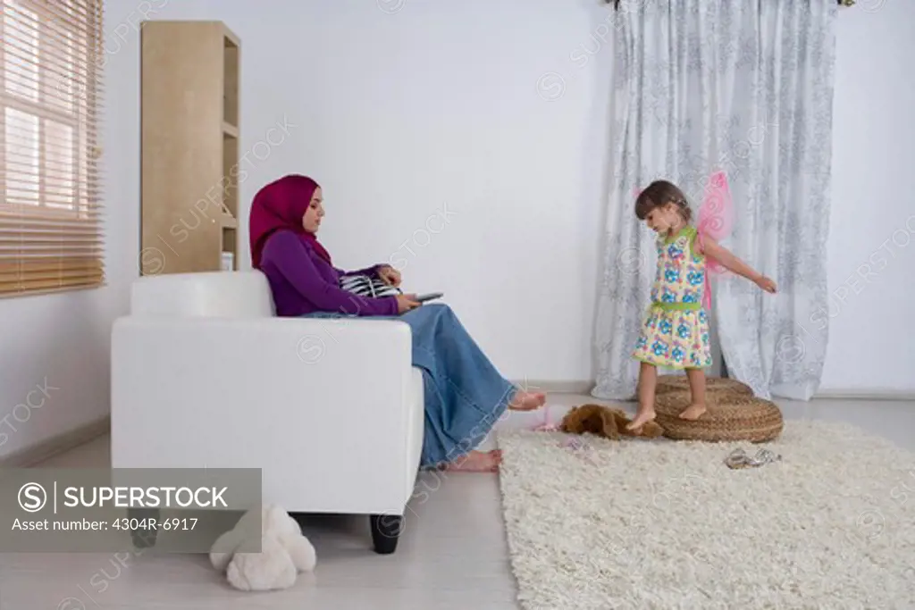 Woman holding the television remote control, daughter playing around