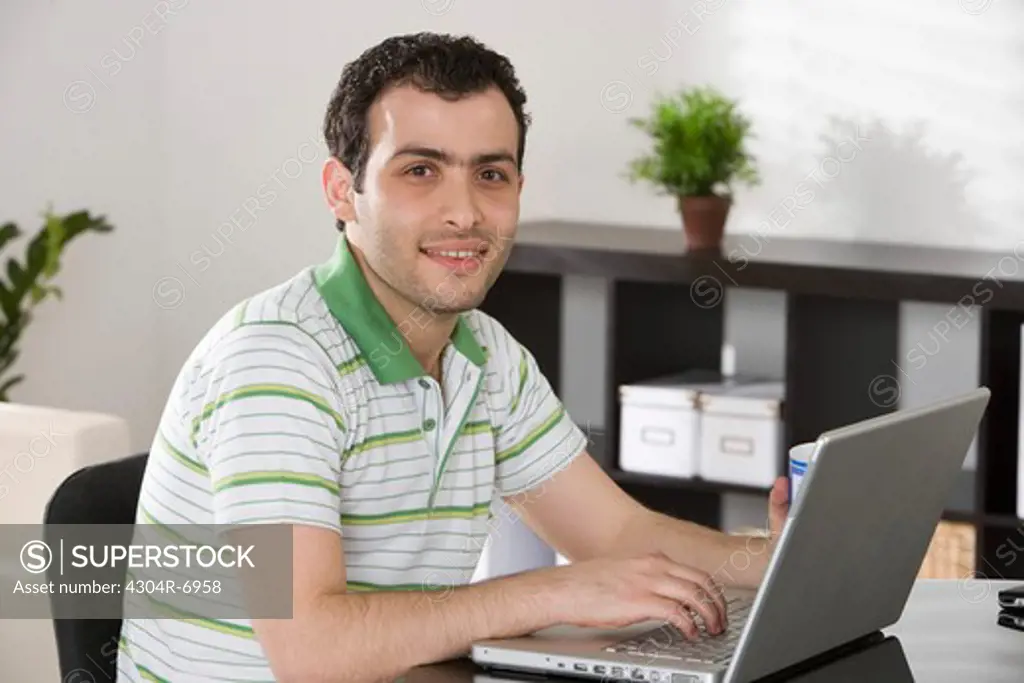 Man sitting in the dining room, typing in his laptop