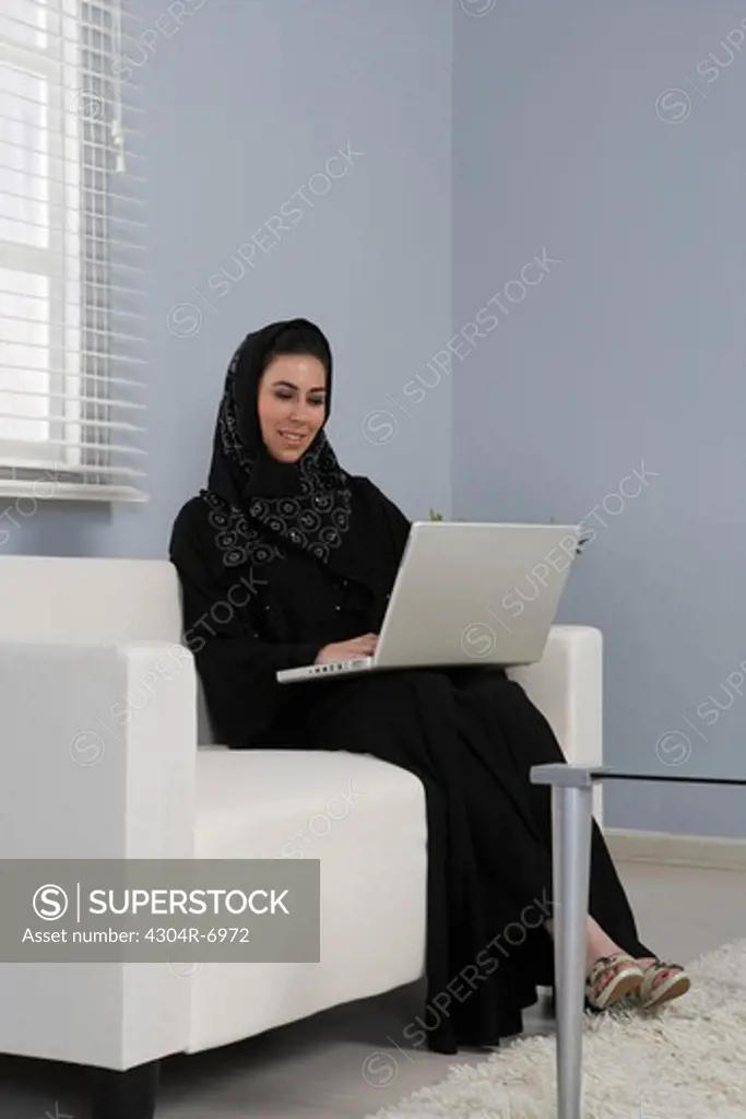 Arab woman sitting on a sofa, working on her laptop