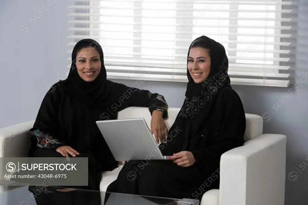 Arab women sitting on a sofa, one woman holding her laptop
