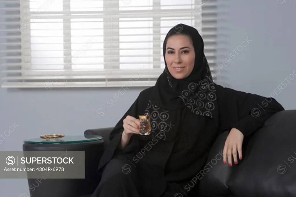 Arab woman holding a cup of tea, sitting on sofa