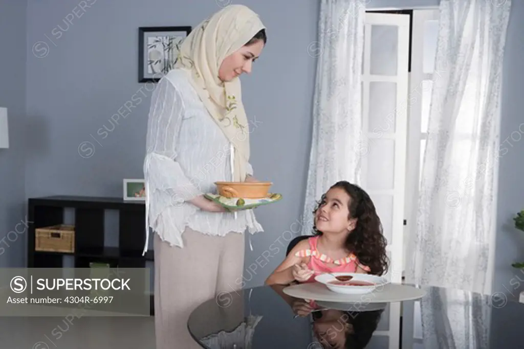 Arab mother serving, girl eating soup