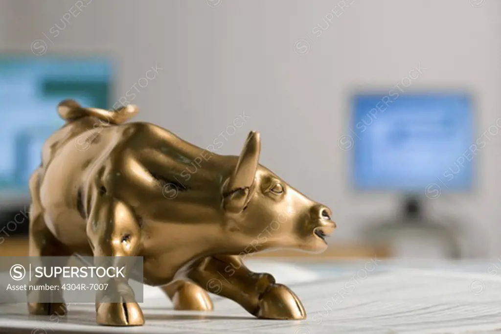 Bull figurine on newspaper, background computers, close-up