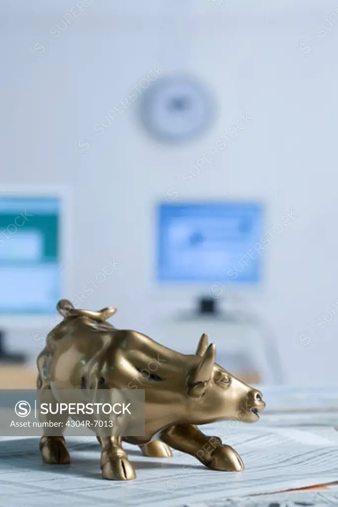 Bull figurine on newspaper, background computer and clock, close-up