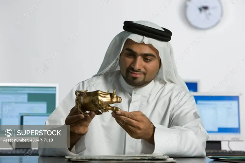 Arab man holding a bull figurine, background computers