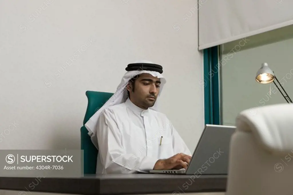 Arab businessman typing on a laptop, sitting at the office