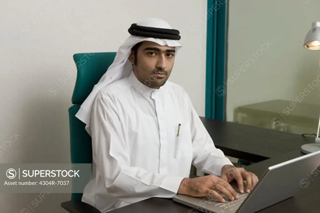 Arab businessman typing on a laptop, sitting at the office