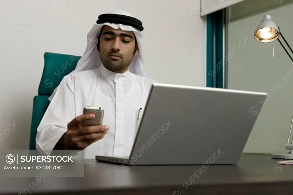 Arab businessman sending SMS, sitting at the office
