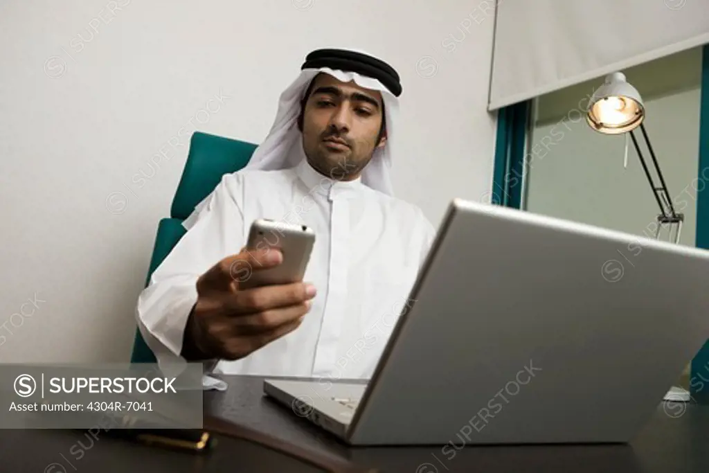Arab businessman sending SMS, sitting at the office