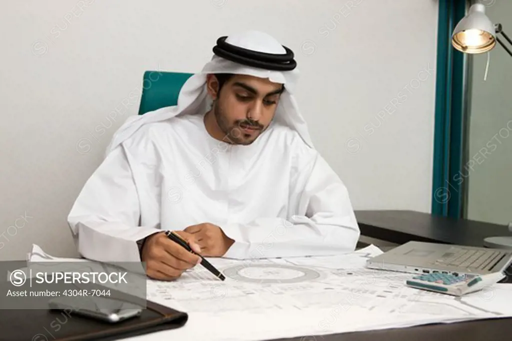 Arab businessman holding a pen, looking at the blueprint