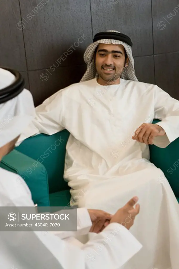 Two Arab businessmen sitting in office, discussing, smiling