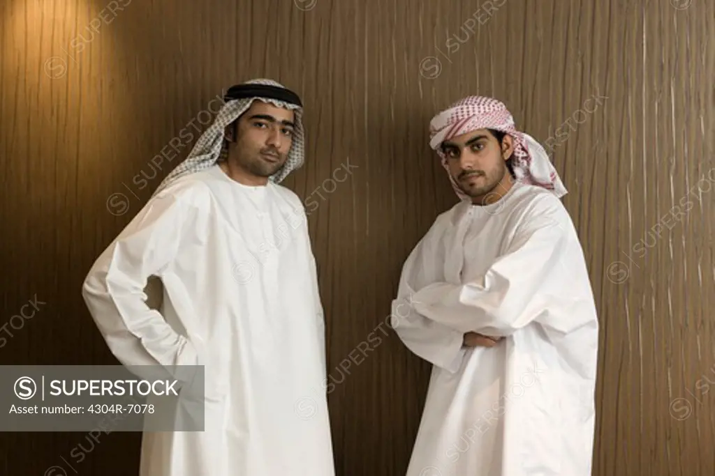 Two Arab men standing near the office wall, portrait