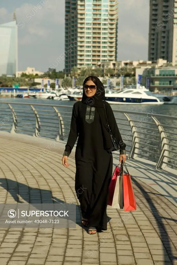 Arab woman with shopping bags, walking at Dubai Marina, UAE