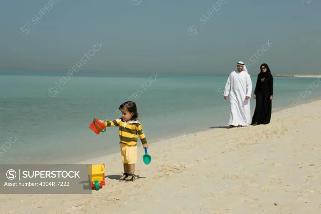 Arab couple watching their son play at the beach