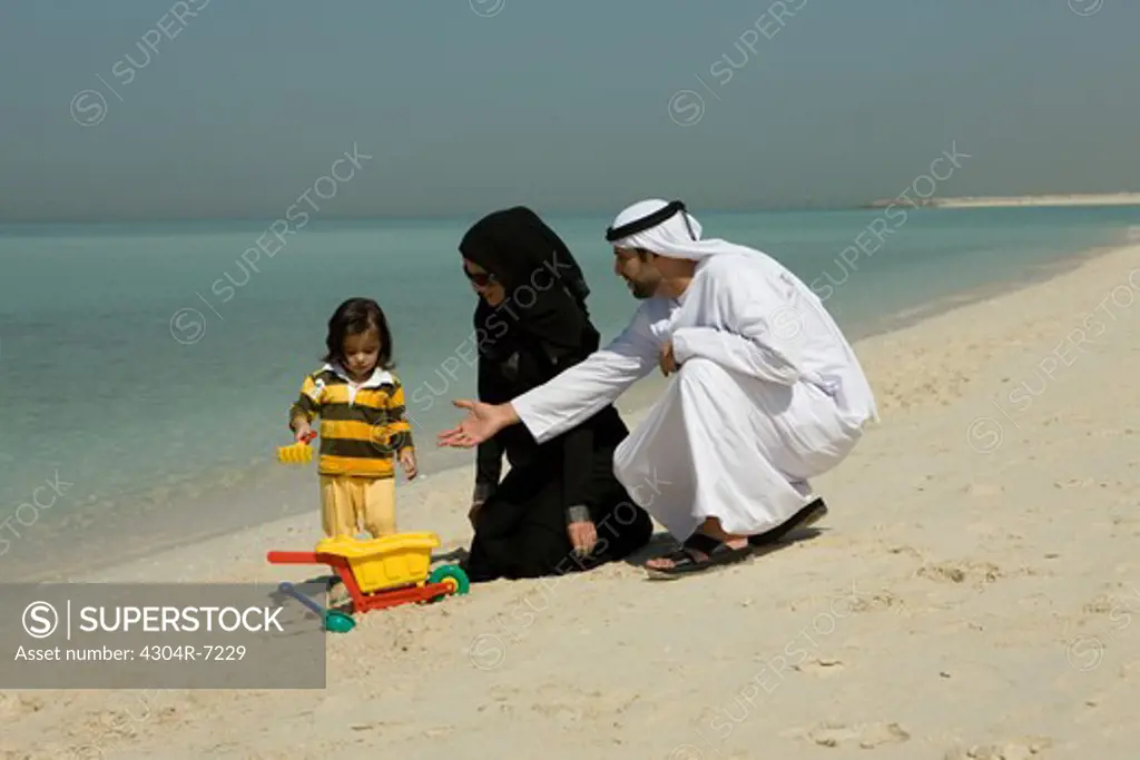 Arab couple playing their son at the beach