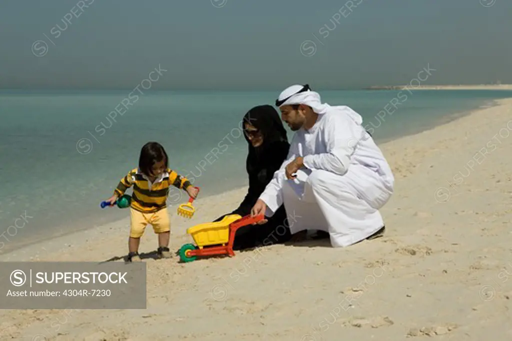 Arab couple playing their son at the beach