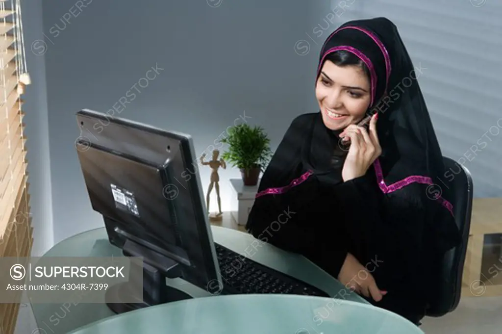 Arab woman using cellphone in front of computer