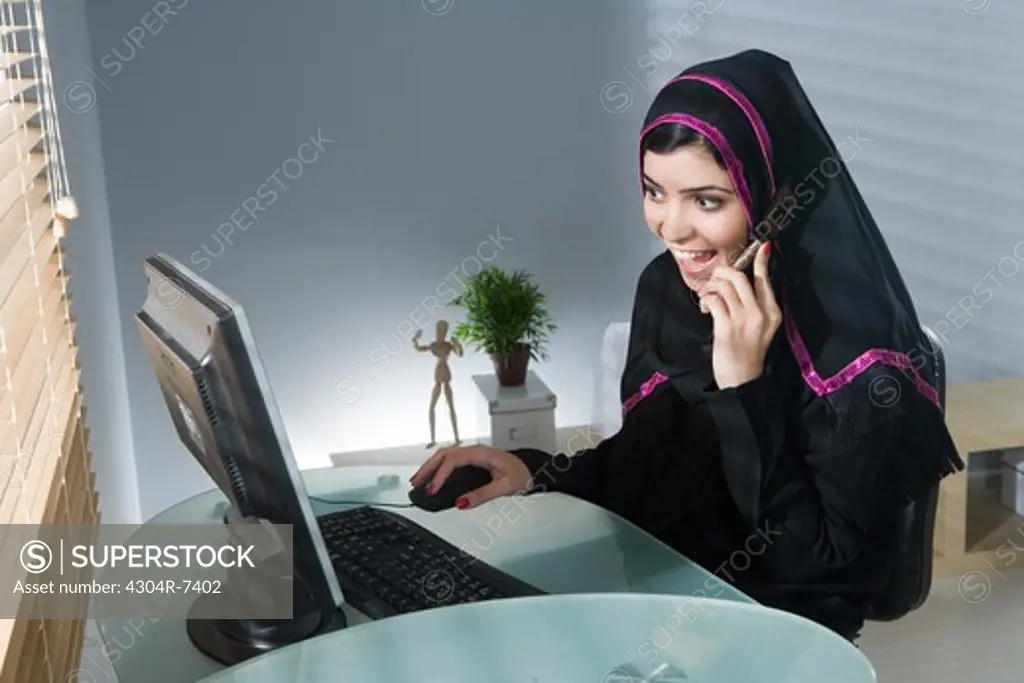 Arab woman using cellphone in front of computer