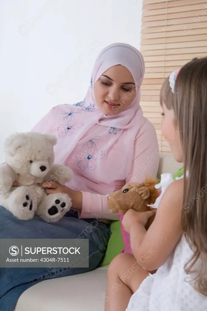 Mother and daughter sitting on sofa, playing with toys