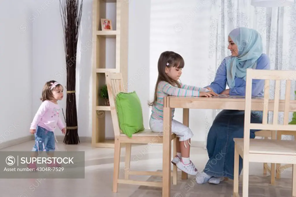 Arab mother with two daughters playing at the dining room