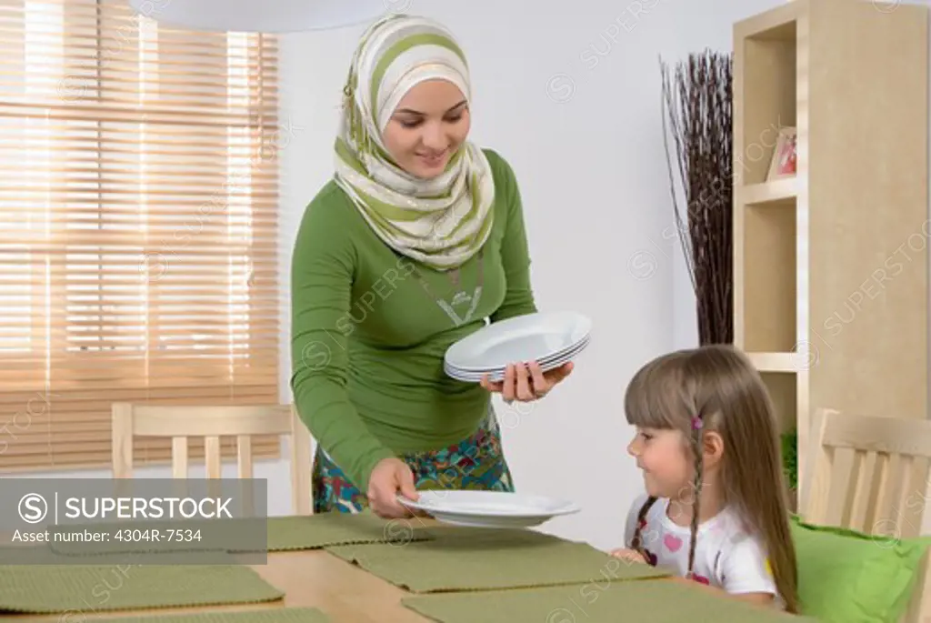 Arab mother and daughter in the dining room, woman setting table