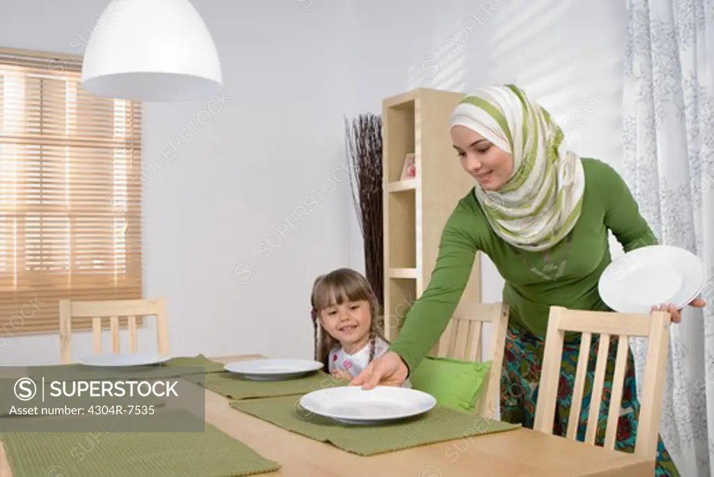 Arab mother and daughter in the dining room, woman setting table