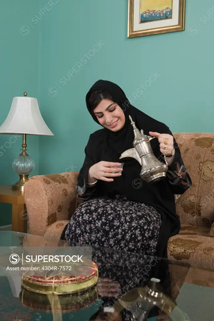 Arab woman holding a teapot, sitting on sofa
