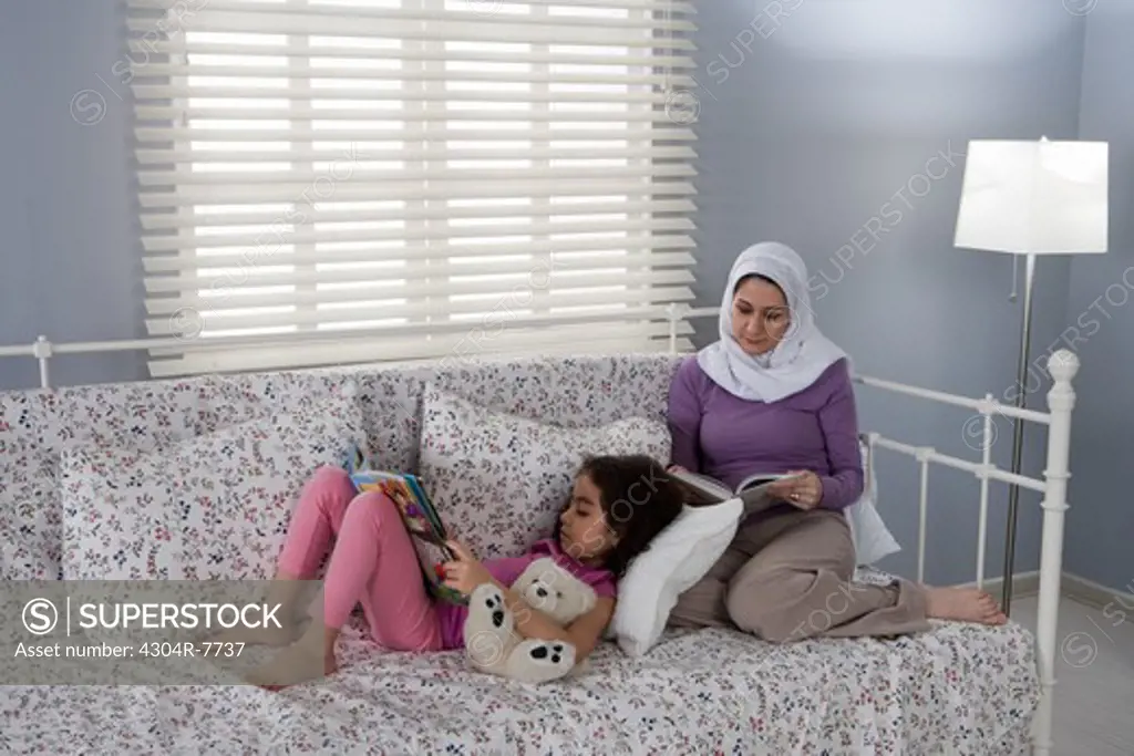 Arab mother and daughter reading book in bed