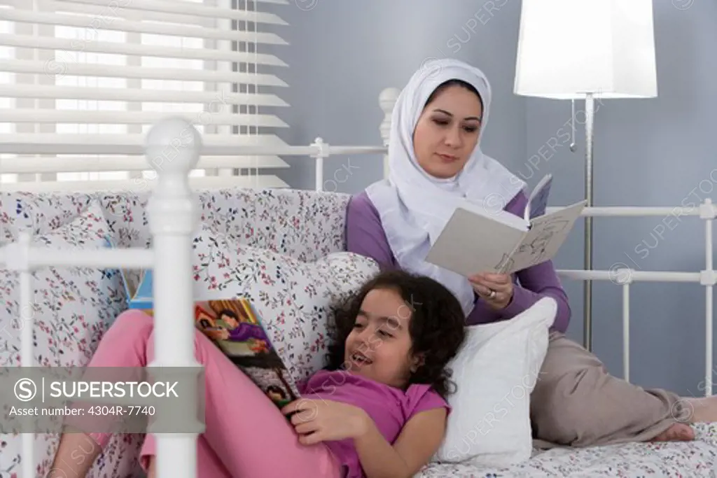 Arab mother and daughter reading book in bed
