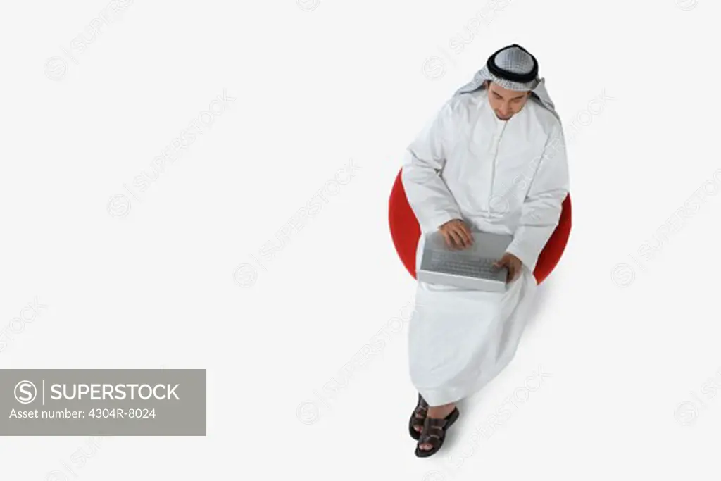 Young man sitting on chair, using laptop, top view