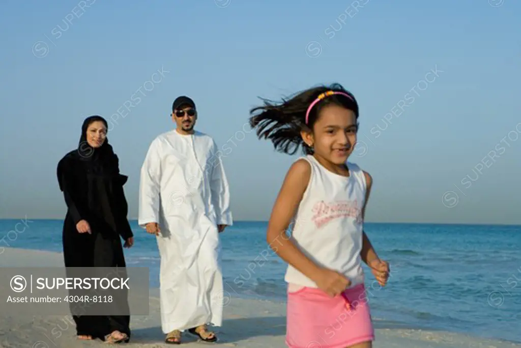 Girl running on beach while parents walking behind, smiling