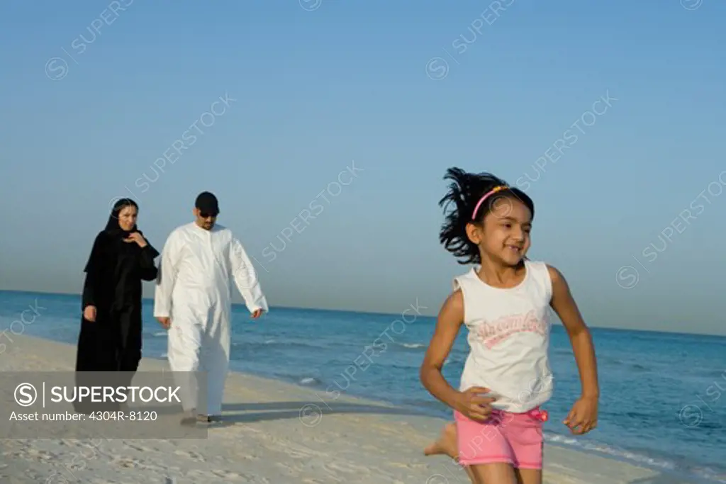 Girl running on beach while parents walking behind