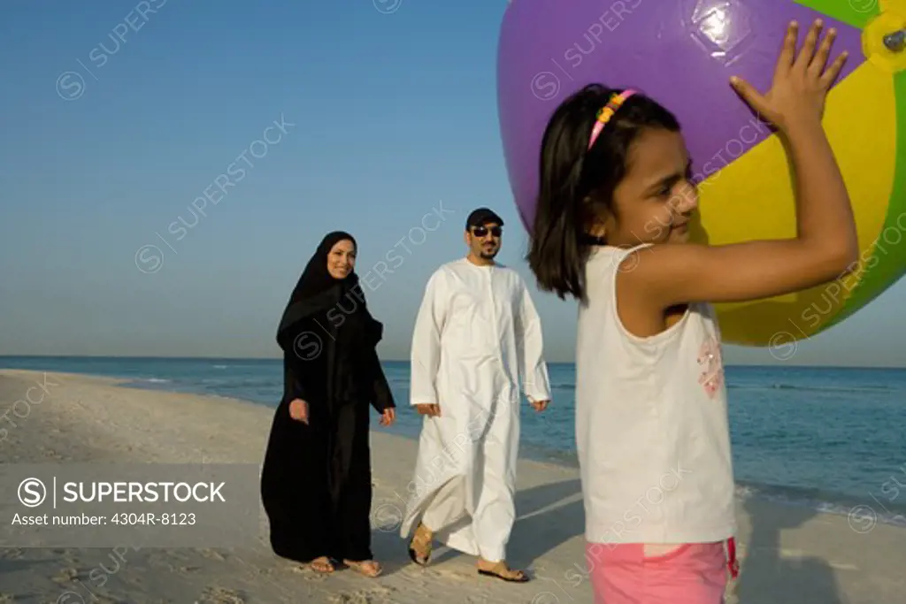 Girl holding beach ball while parent walking in background