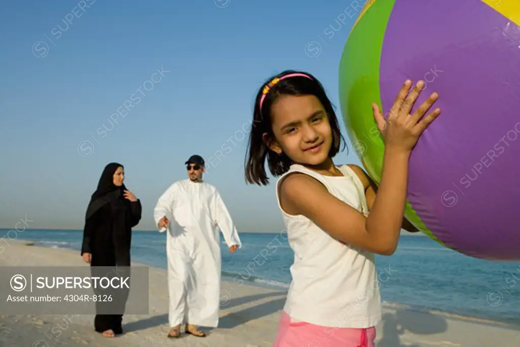 Girl holding beach ball while parent walking in background, portrait