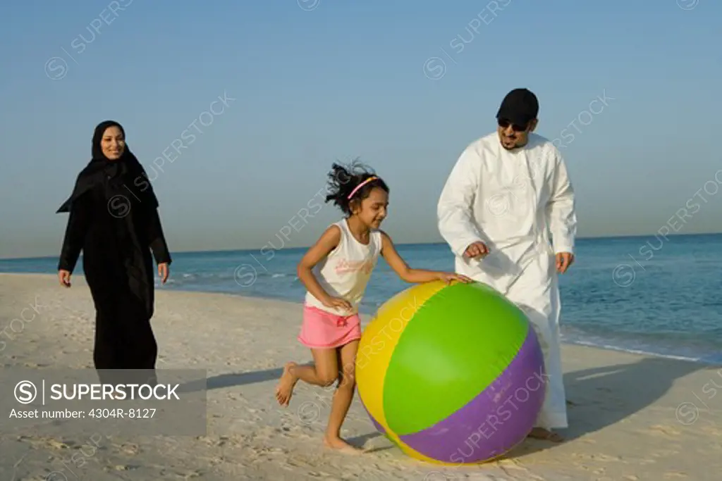 Girl playing beach ball with father while mother walking behind on beach