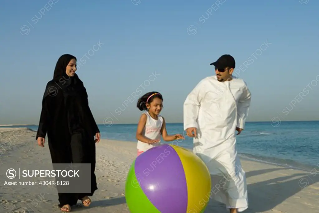 Girl playing beach ball with parents on beach