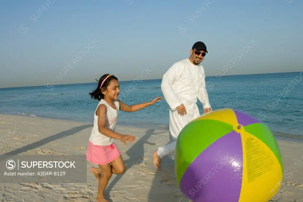 Girl playing beach ball with father on beach, side view
