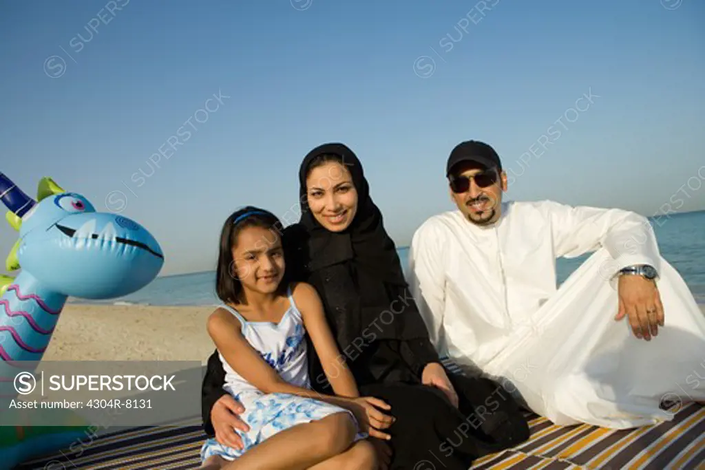 Girl sitting with parents on beach, smiling, portrait