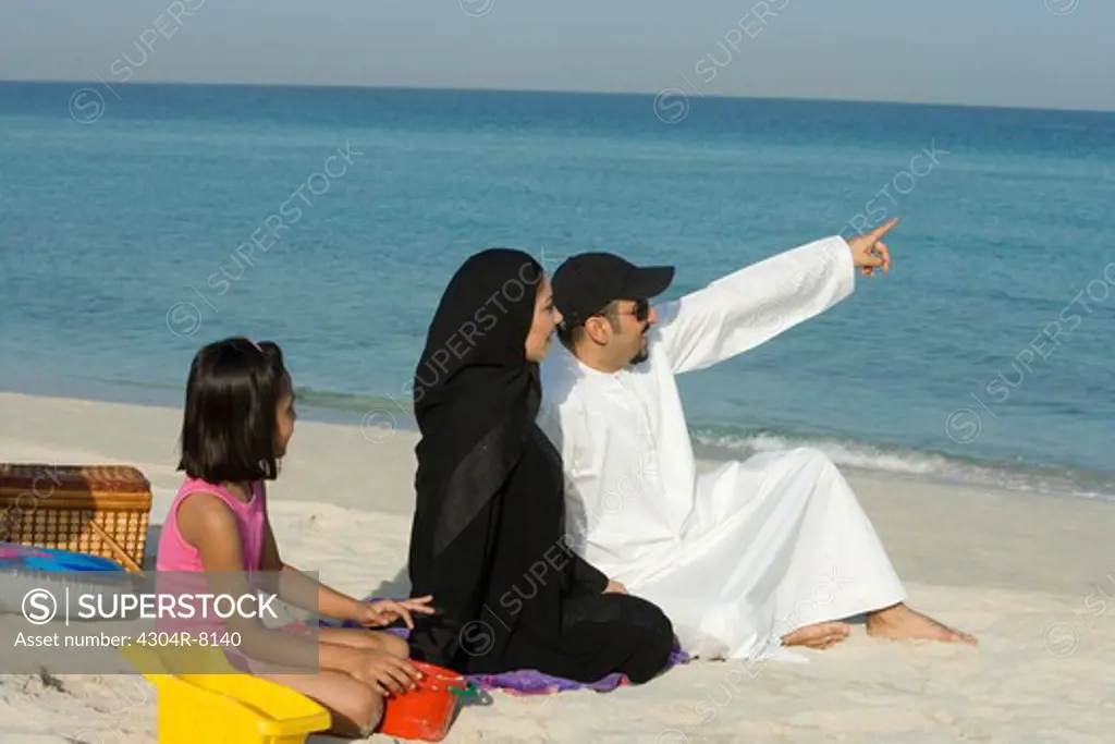 Girl sitting with parents on beach, side view
