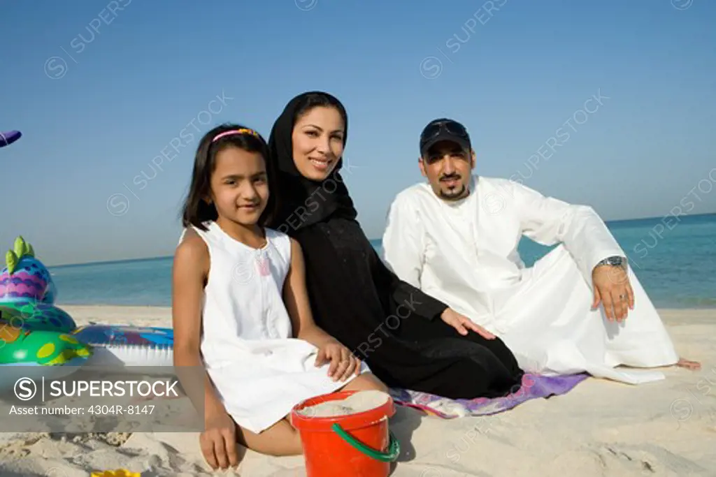 Girl sitting with parents on beach, smiling, portrait