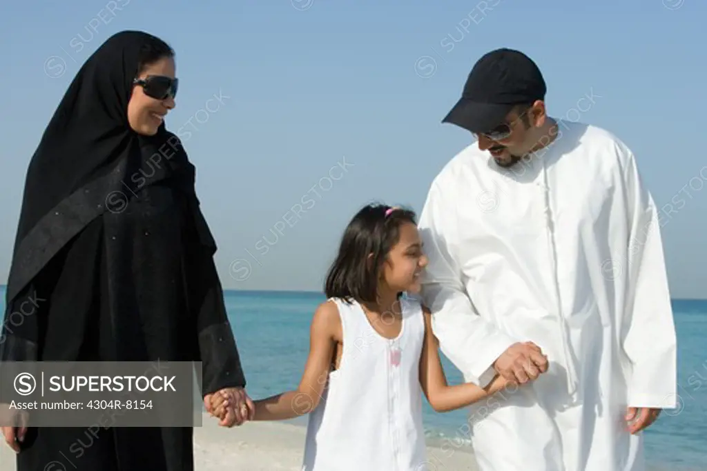 Girl walking with parents on beach, smiling