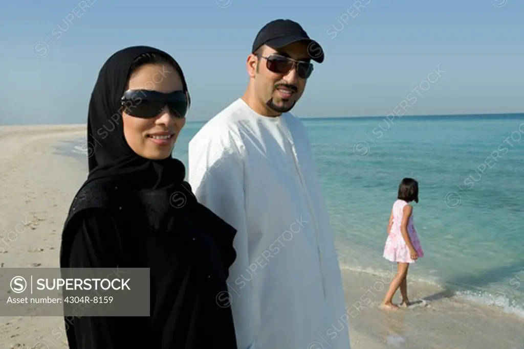 Young couple with daughter on beach, smiling, portrait