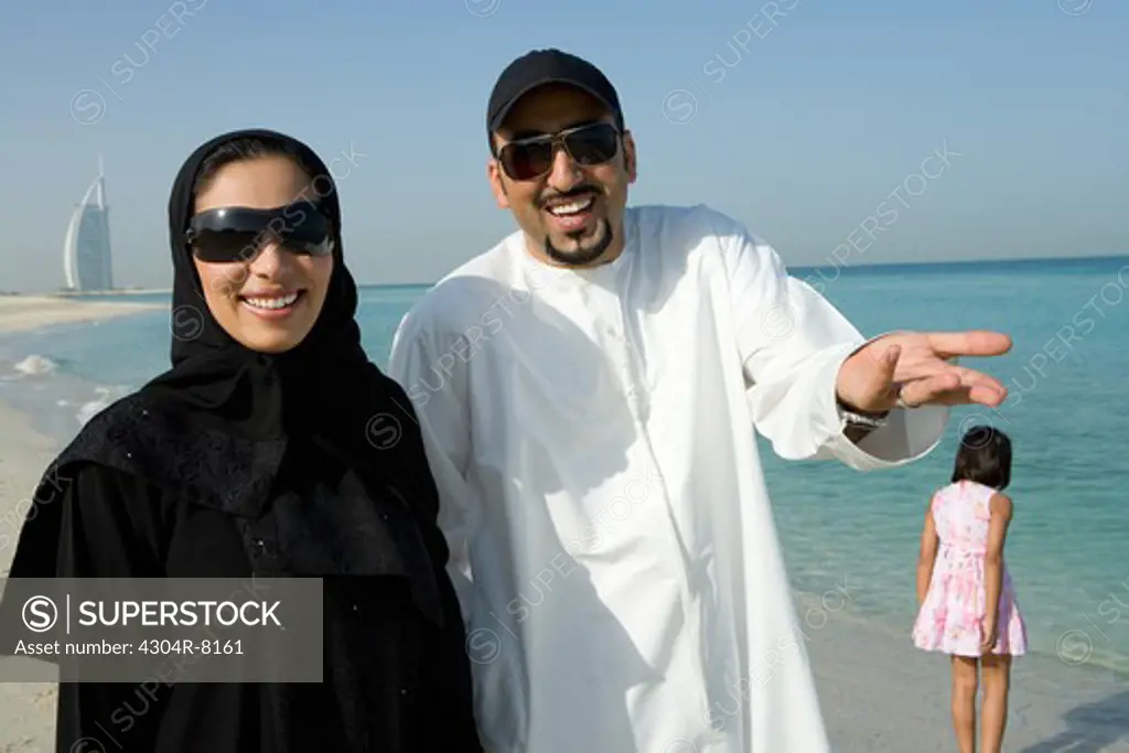 Young couple with daughter on beach, smiling, portrait