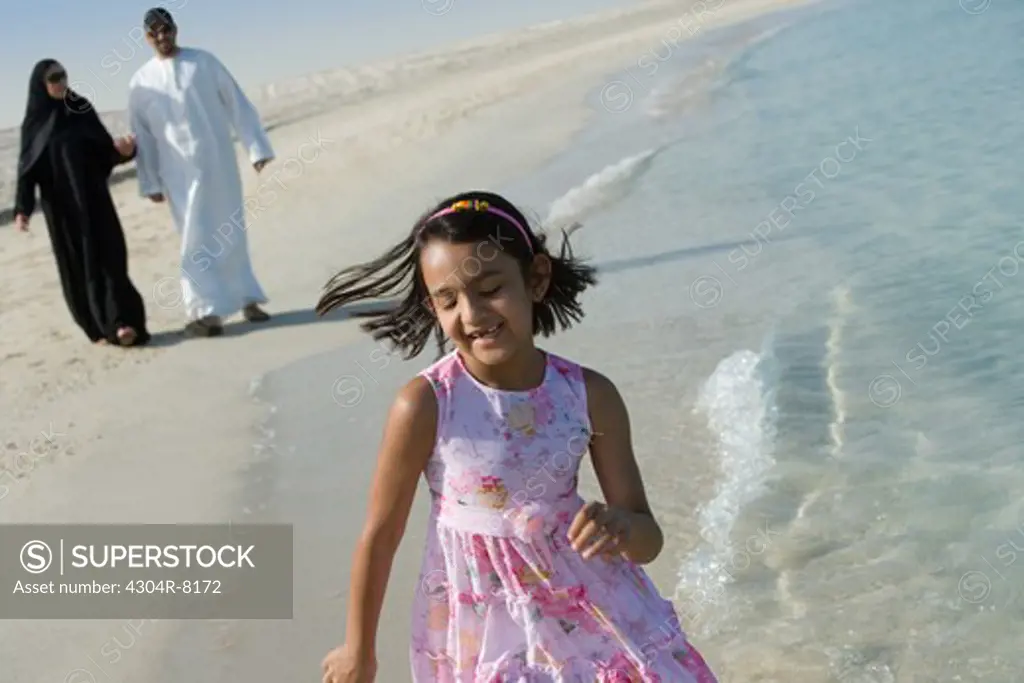 Girl running on beach while parent walking behind