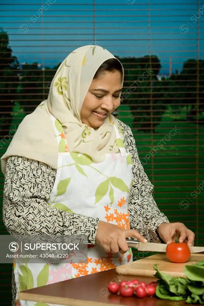 Mid adult woman cutting tomato, smiling, portrait.