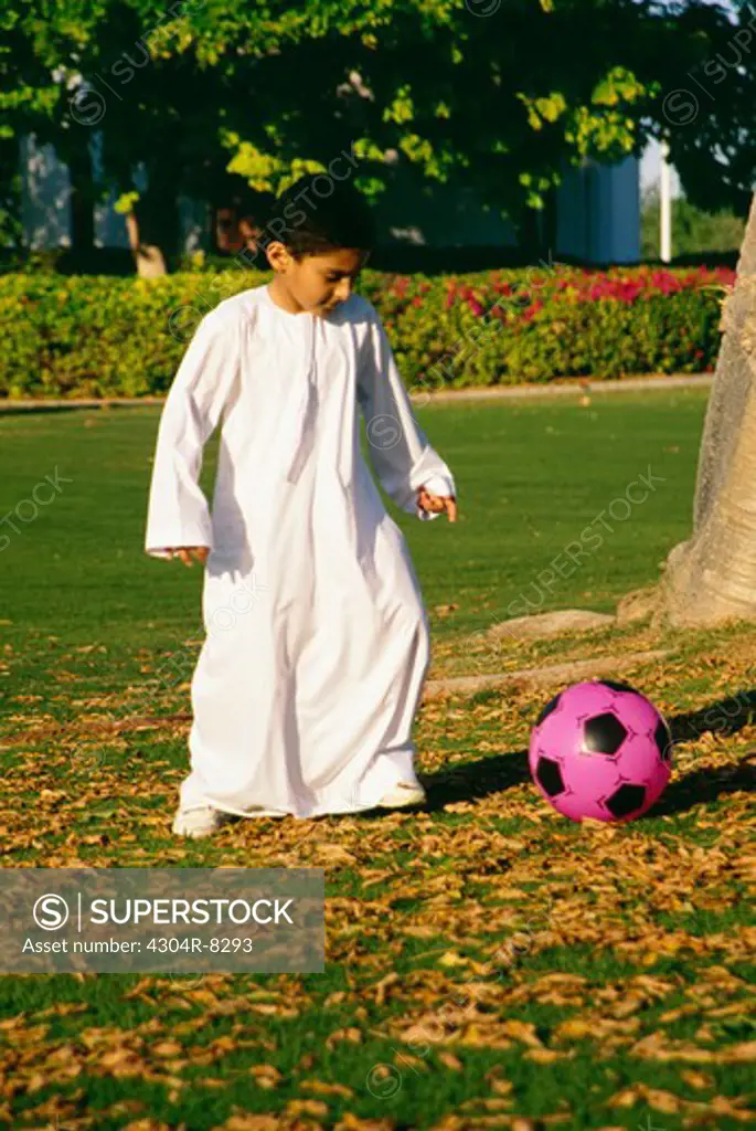 A small boy in traditional dress plays football in the park.