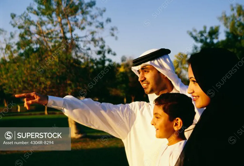 A father points out at something while his wife and son look on.