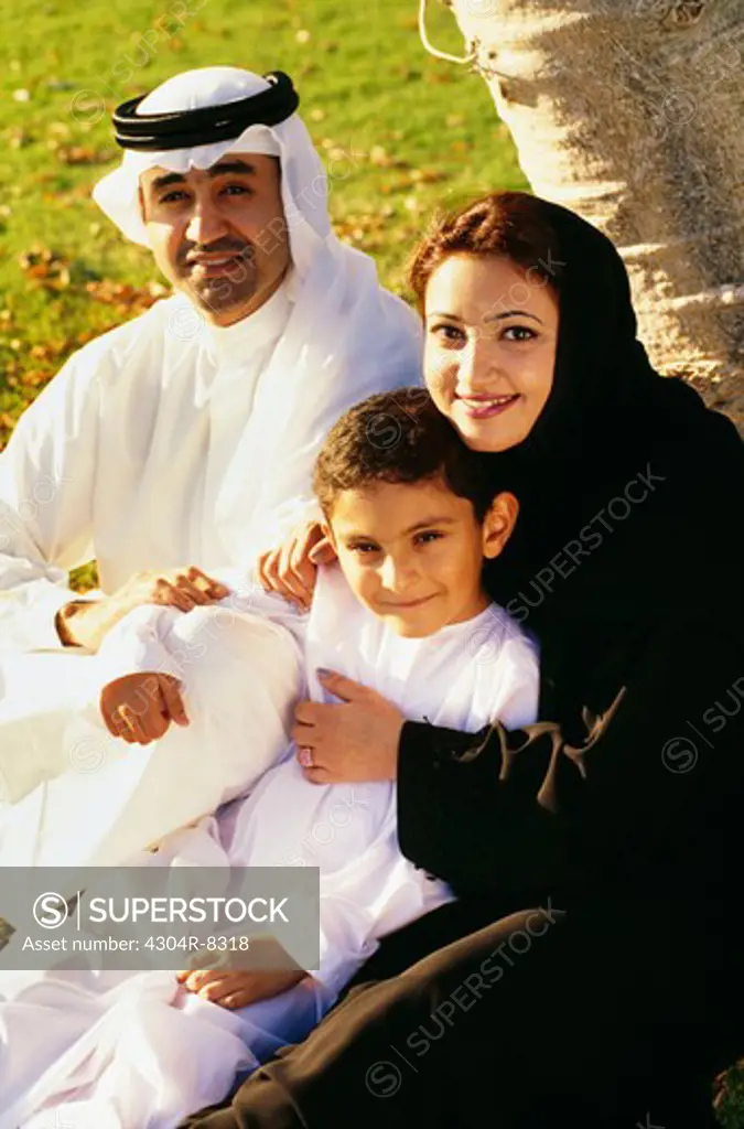 An Arabian family shares a light moment as they sit under the tree and smile at the camera.