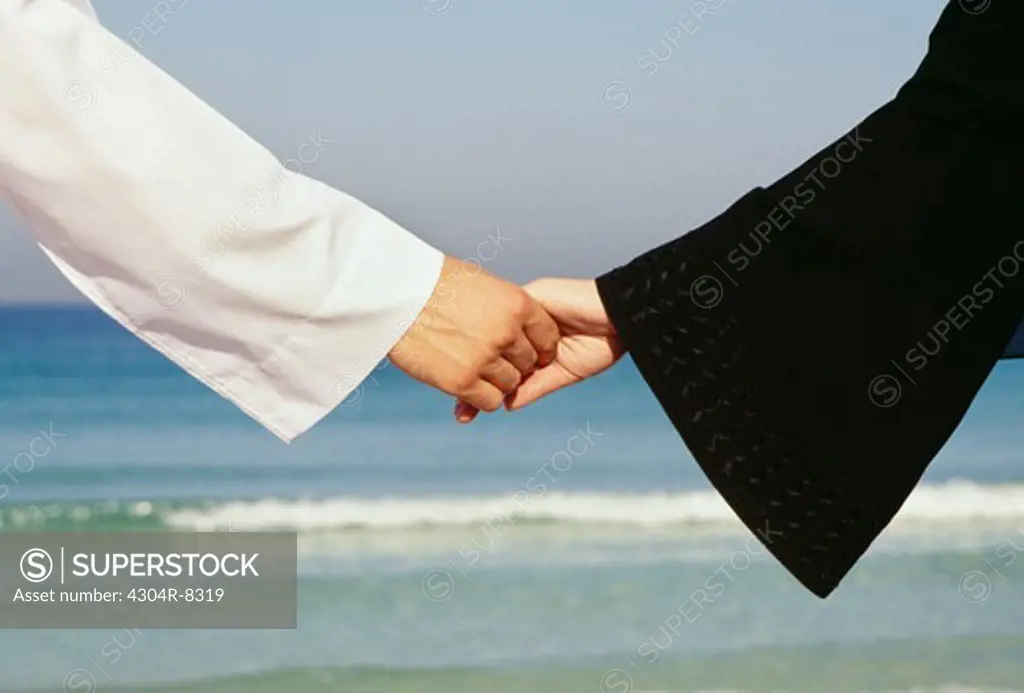 A couple clasp each others hand at the seashore.
